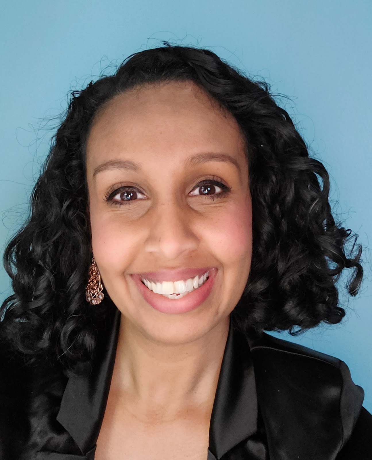 Headshot of Sarah de Freitas, dressed in black against a blue background.