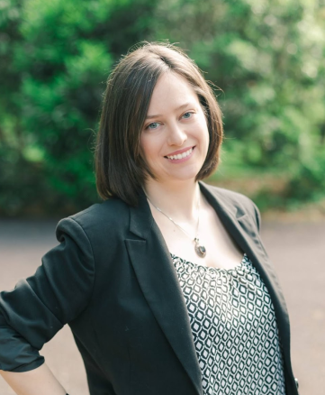 Headshot of Allie Emmerich wearing a black blazer with nature in the background,