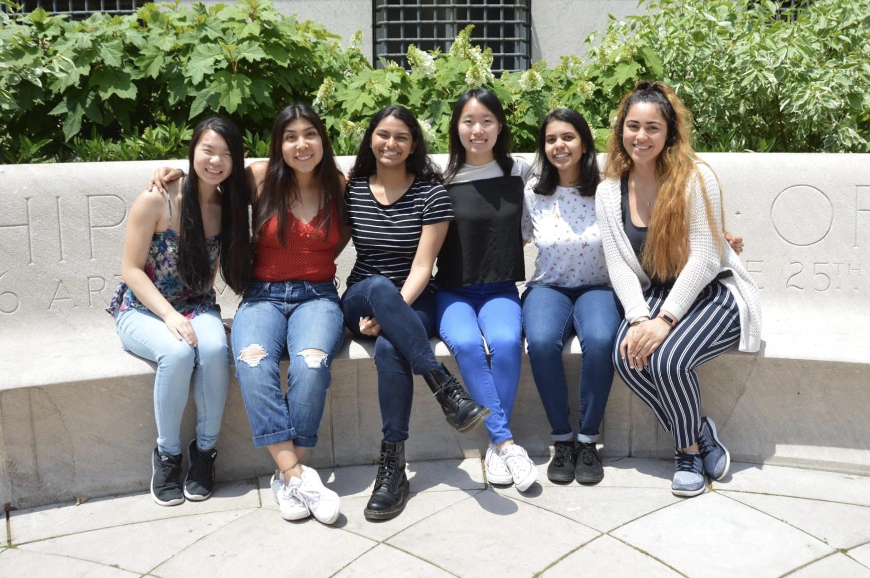 Six young women sitting together on a bench.