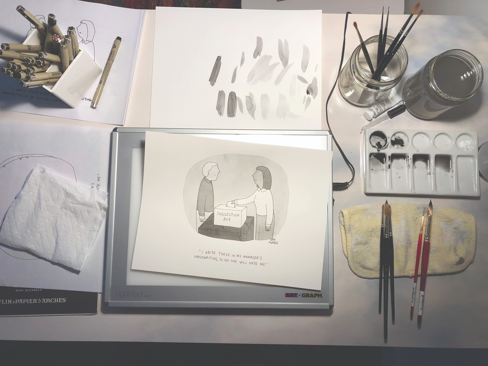 Photo of Hwang's workspace, with an in-progress watercolor cartoon surrounded by watercolor materials