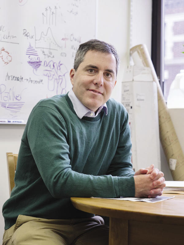 A photo of Professor Brian Mailloux sitting at a desk wearing a green sweater