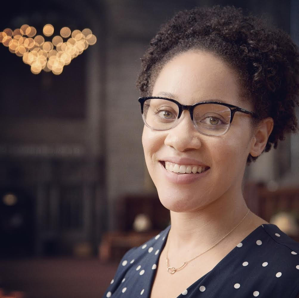 Jalisha Jenifer positioned to the right wearing glasses with chandelier in background