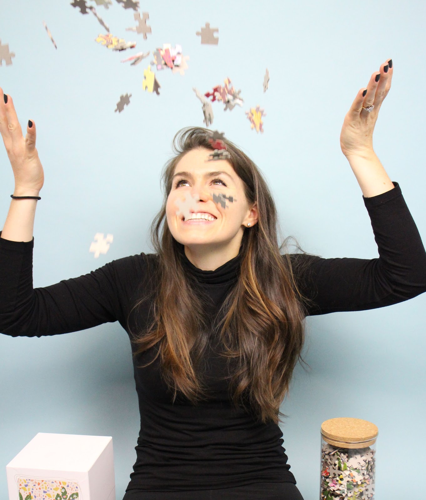 Kaylin Marcotte dressed in black against a light blue background throwing puzzle pieces 