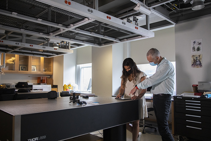 A student and her research mentor stand in a laboratory both looking at a piece of paper on a big table