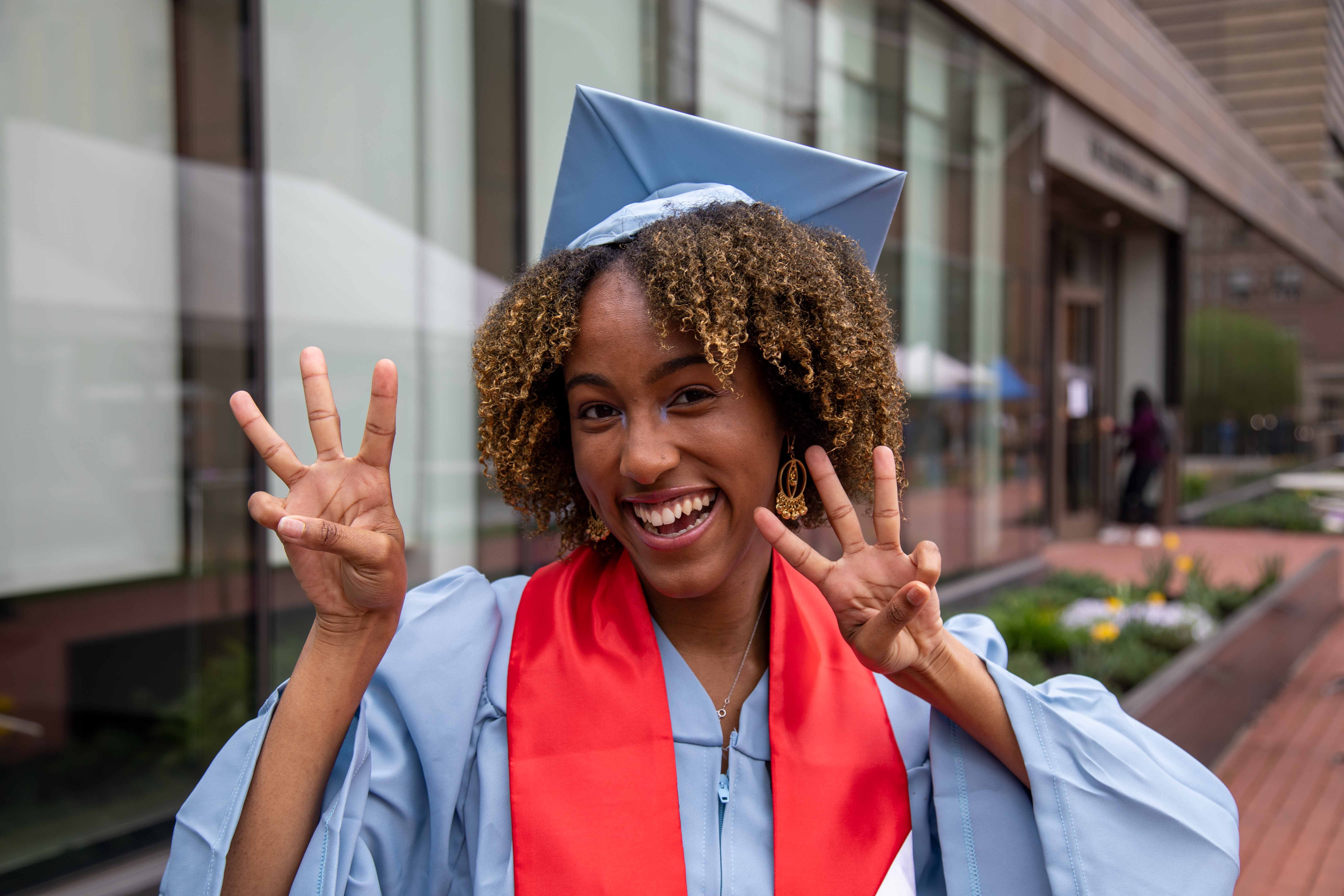 Tonika Henry in her cap and gown in front of Milstein holding up three fingers on each hand.