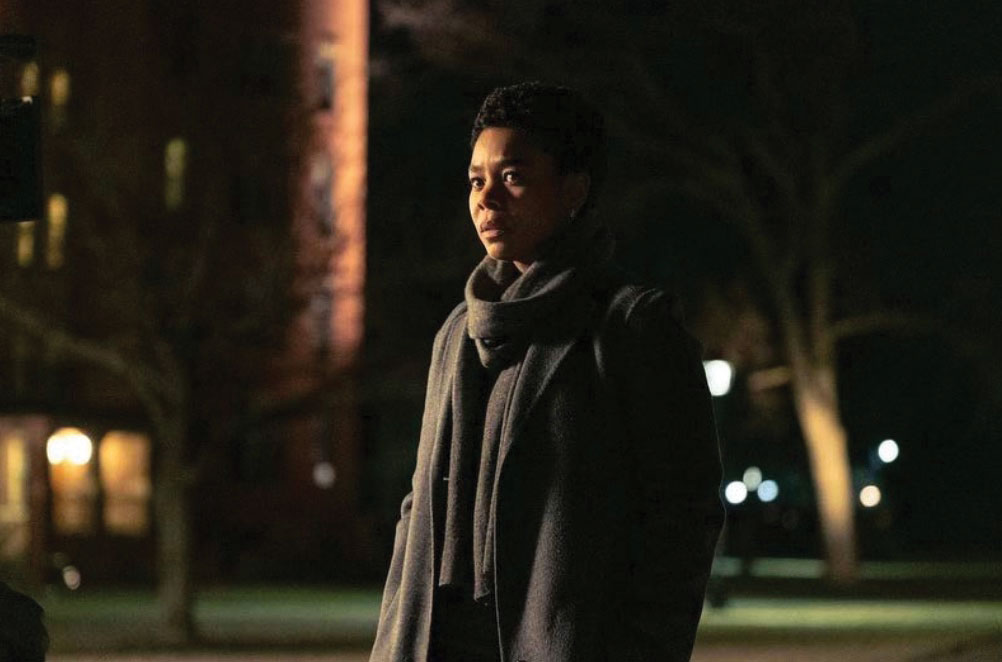 Film still of a Black woman standing in the street under streetlights from the film Master