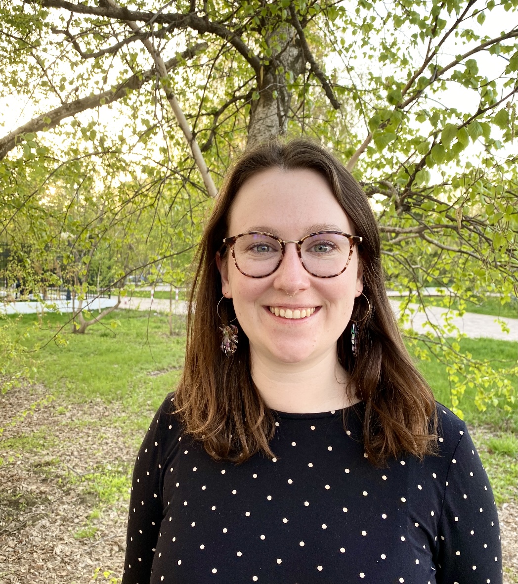 Aly standing outside in front of a tree wearing glasses and a black and white polka dot shirt