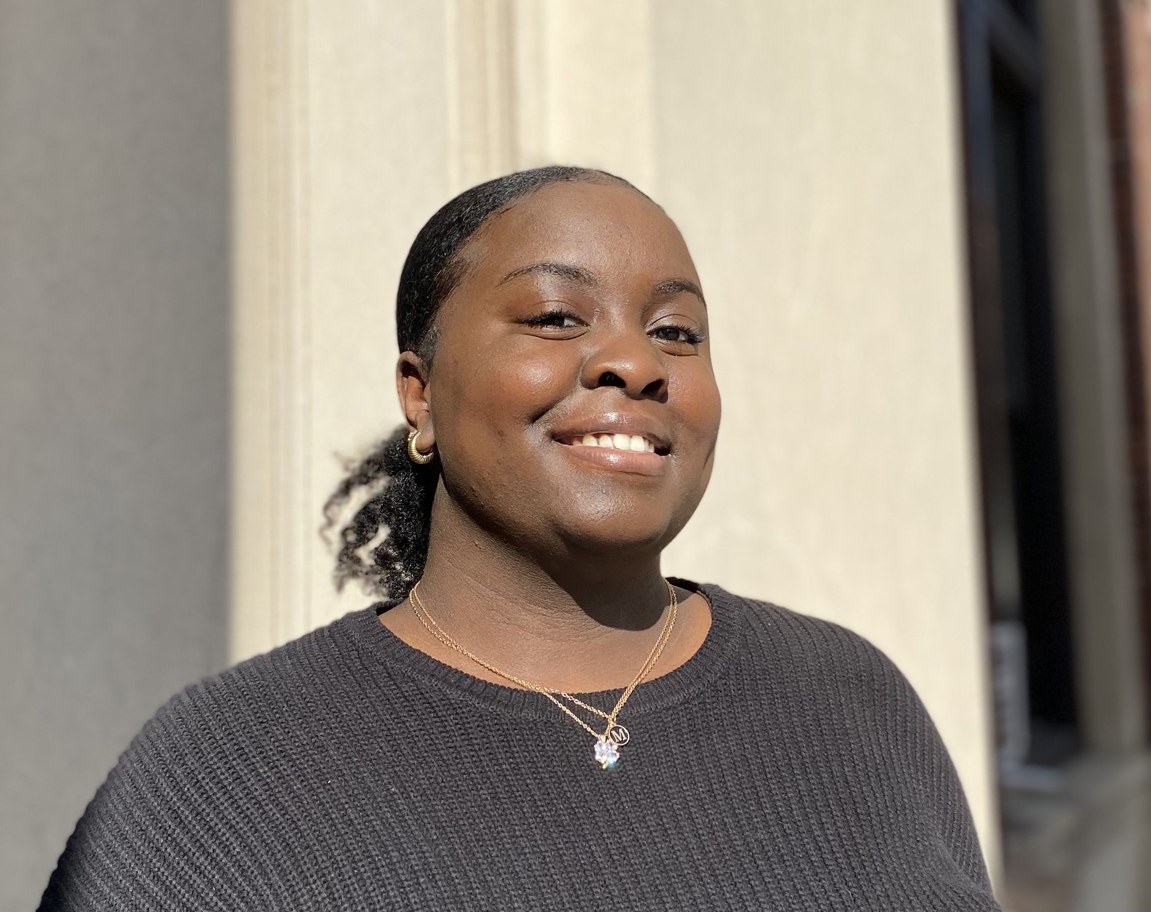 Maya Darville wearing a black sweater standing in front of one of the columns of Barnard Hall