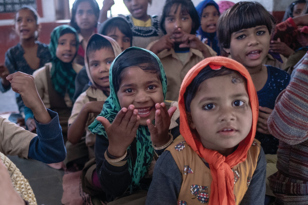 Many young school kids sitting together, facing front, in Deogarh, India