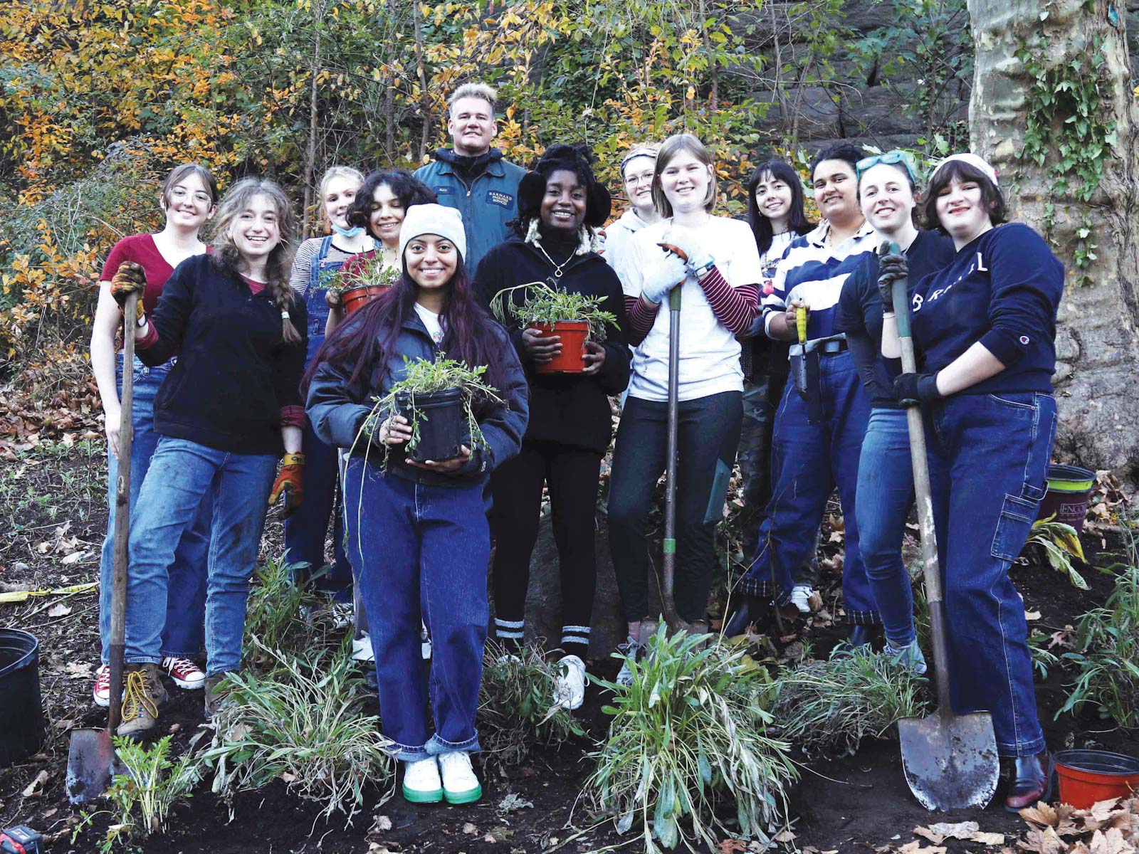 13 people stand with shovels and plants outside