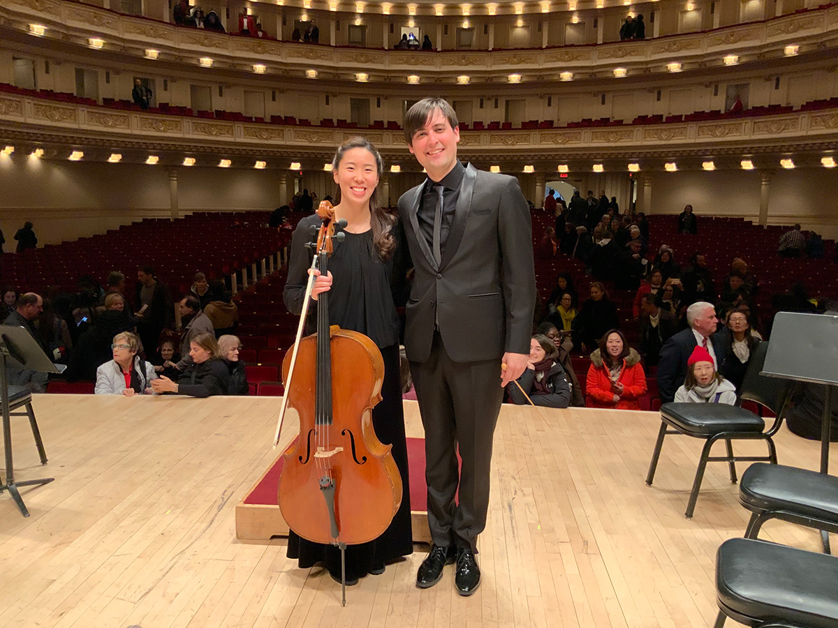 Woman wearing black dress holding cello standing next to man wearing black suit