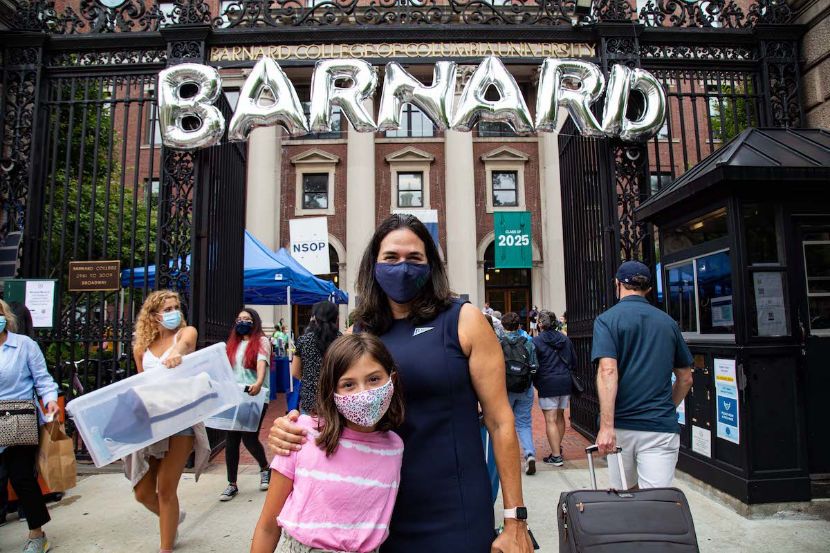 Woman wearing blue dress hugs young girl in front of Barnard Hall