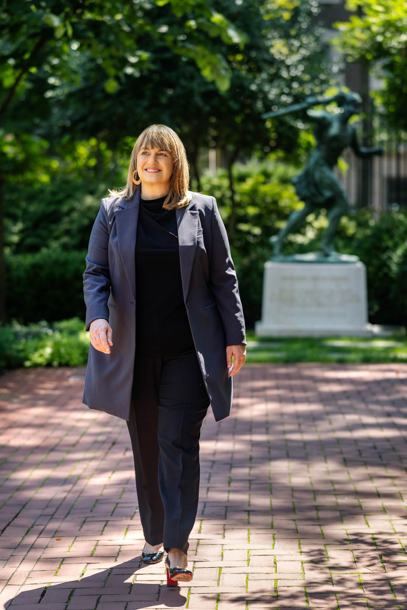 Laura Rosenbury walking on campus the athena statue is behind her