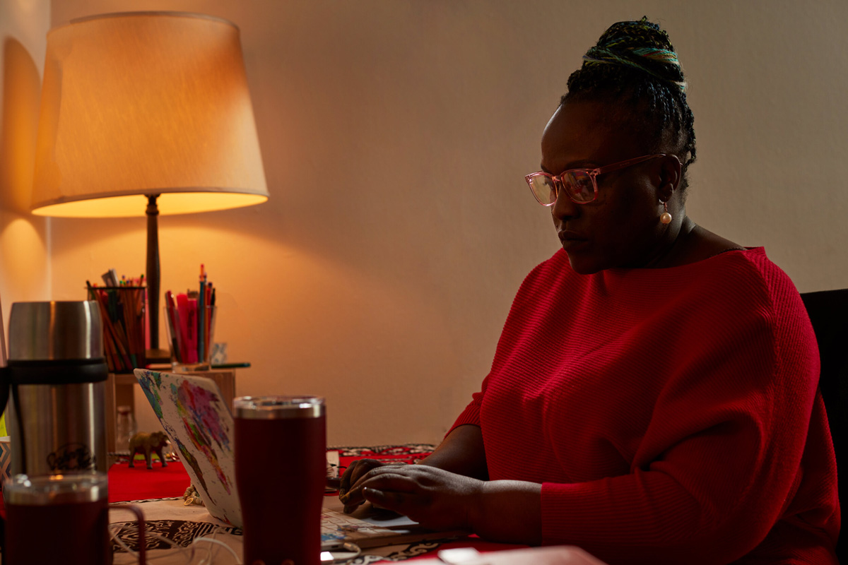 Playwright Achiro P. Olwoch in red top typing at the desk