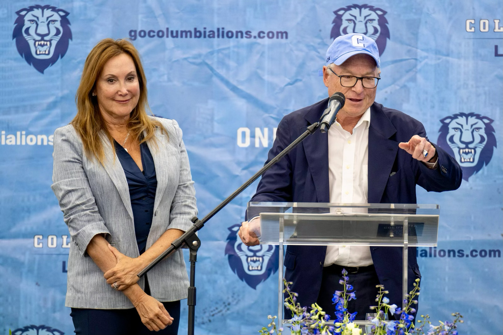 Woman and man wearing a blue baseball stand at a microphone