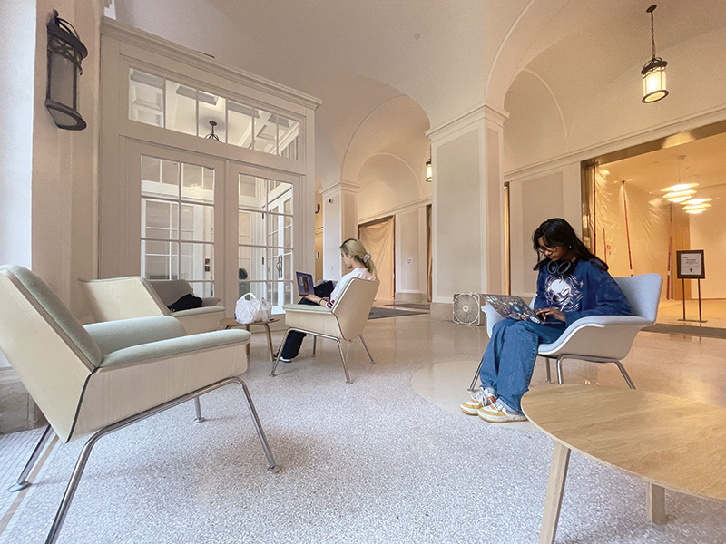 two women sit with laptops on modern chairs in restored lobby 