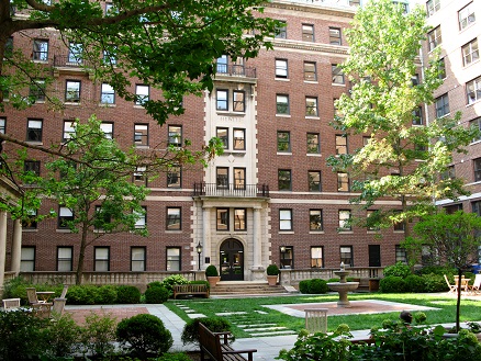 Shows a grassy field with fountain in the middle some pavers, surrounded by tall dormitory buildings.