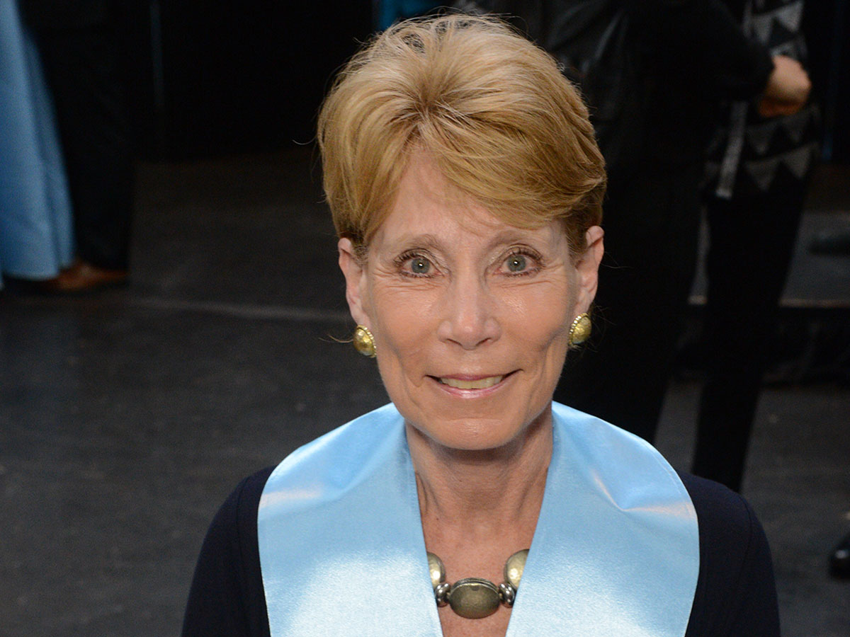 Older woman with short blond hair wearing blue sash around neck.