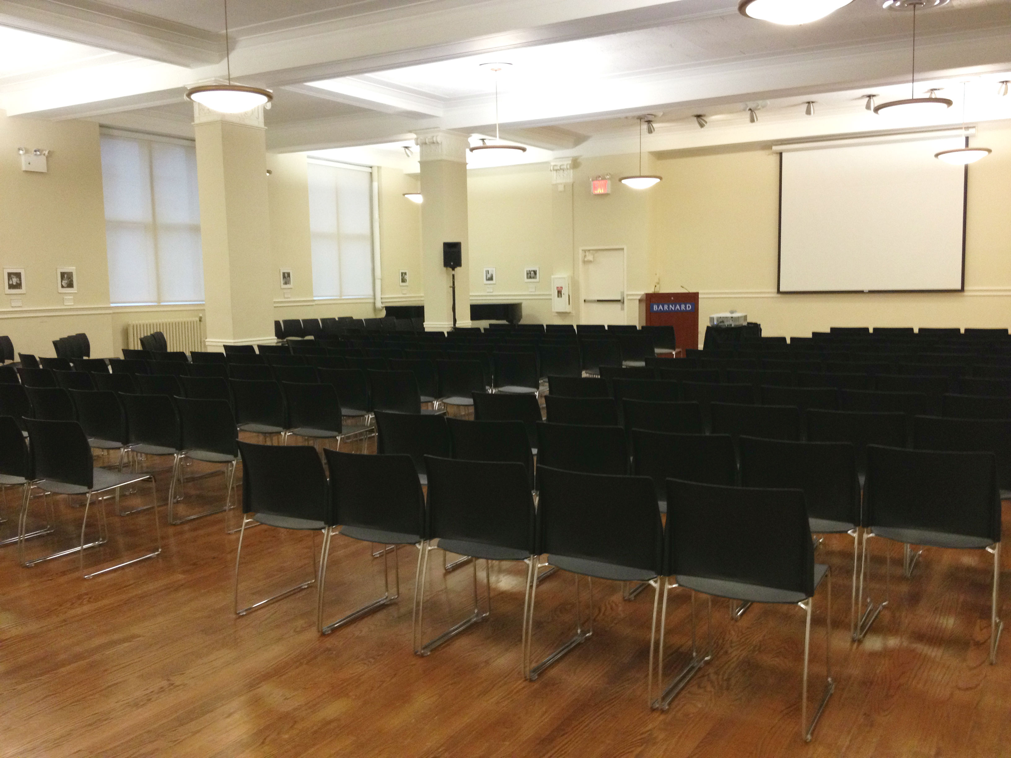 white room with rows of black chairs and wood floor.