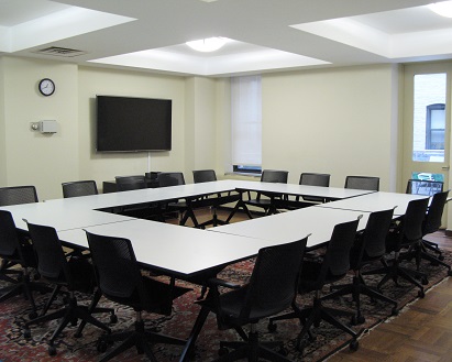 shows AV monitor on wall, black rolling chairs around an open-square table with rug.