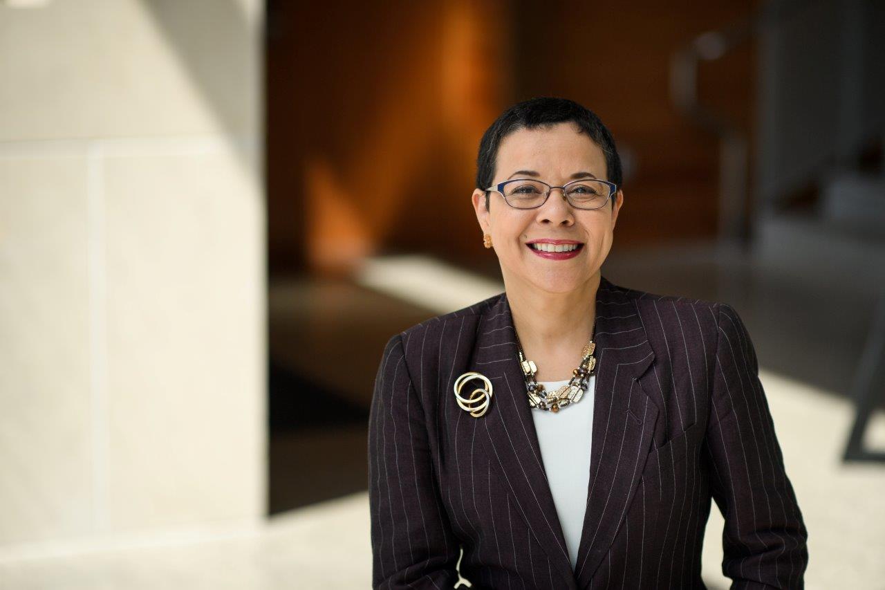 Woman with short curly dark hair wearing dark suit.