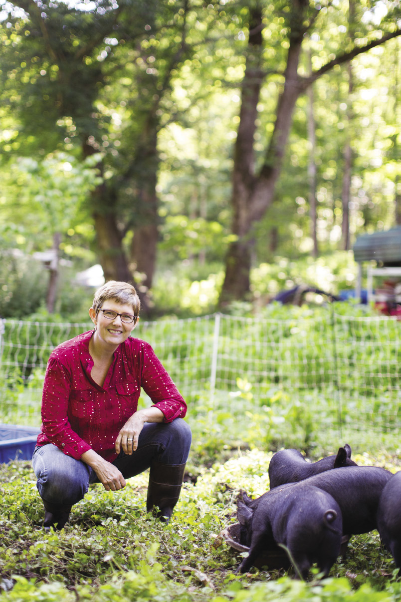 Crystal Cook Marshall ’94 in a field with black piglets