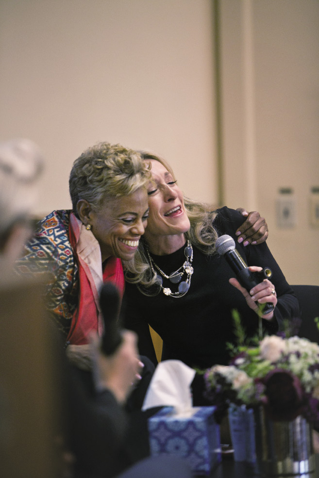 A Black woman gives a white woman a one-armed hug