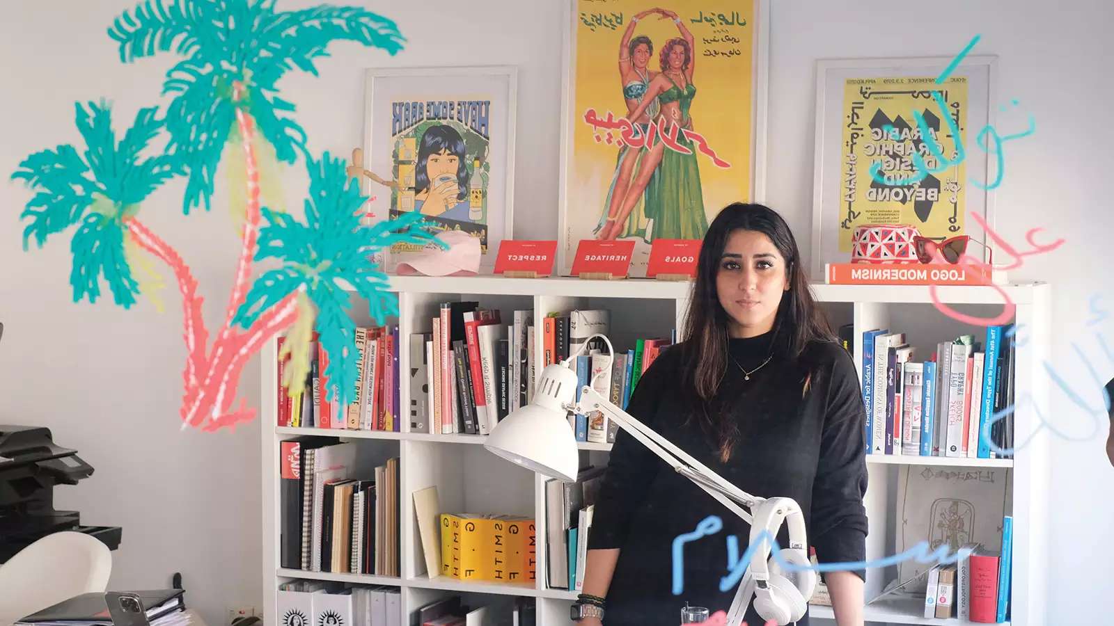 Woman with dark hair and dark shirt standing in front of desk inside a design studio