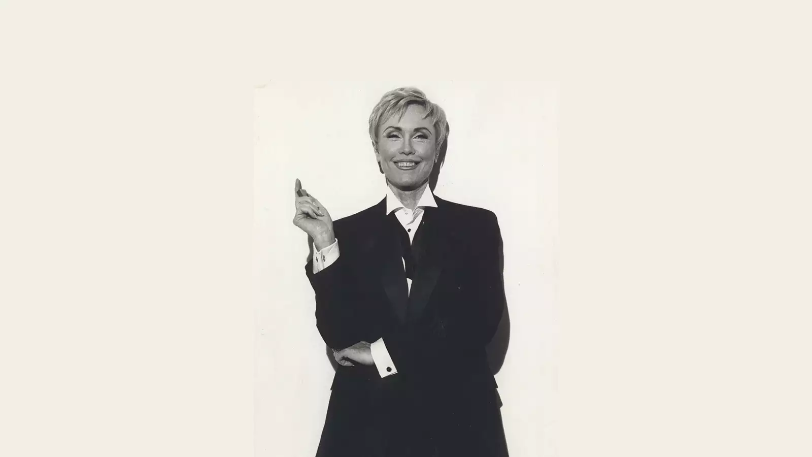 Nancy Friday shot on a white background right arm up resting on folded left arm. She sports a blond pixie hair cut.