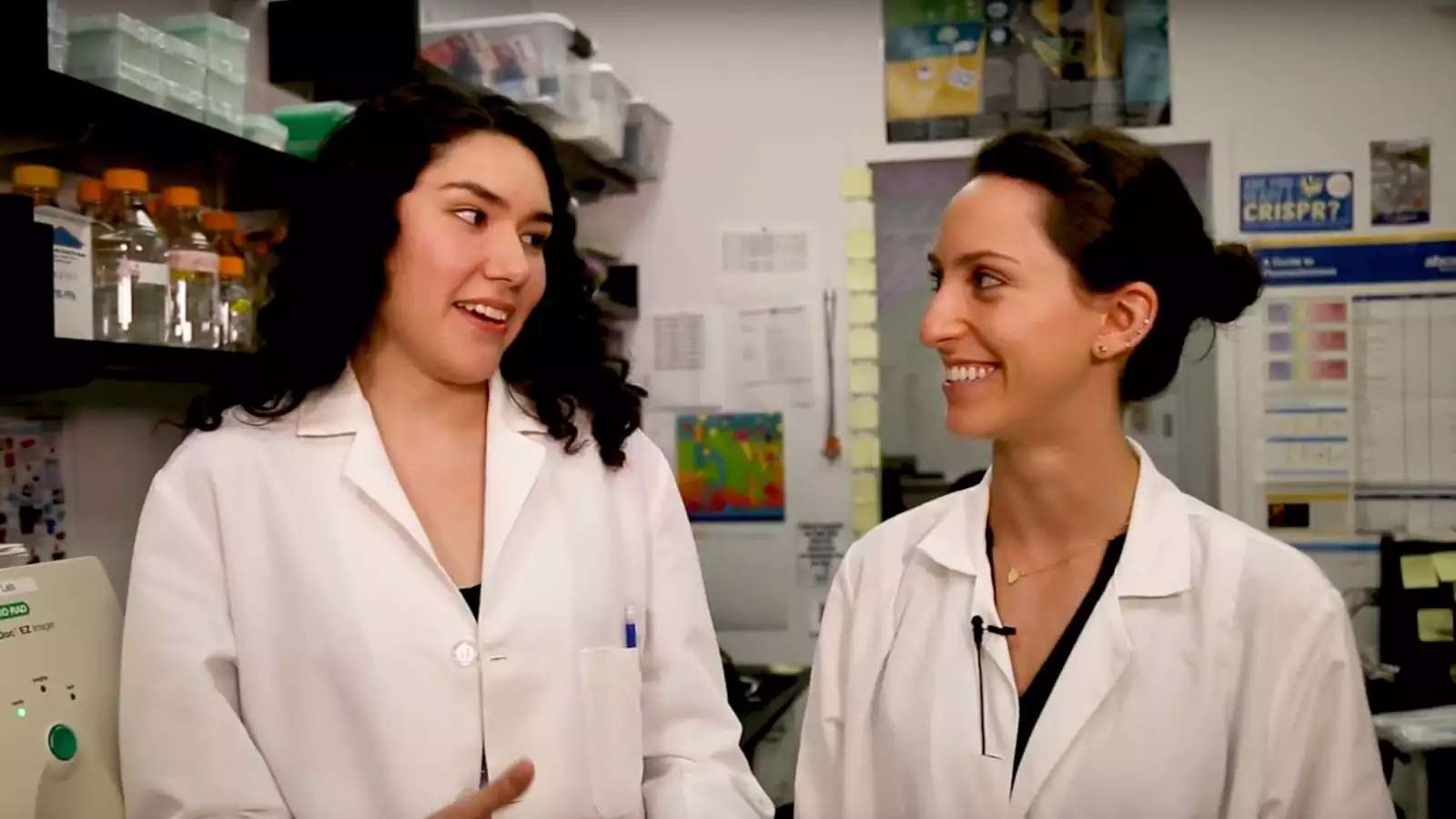 Two young women in lab coats speaking in a science lab