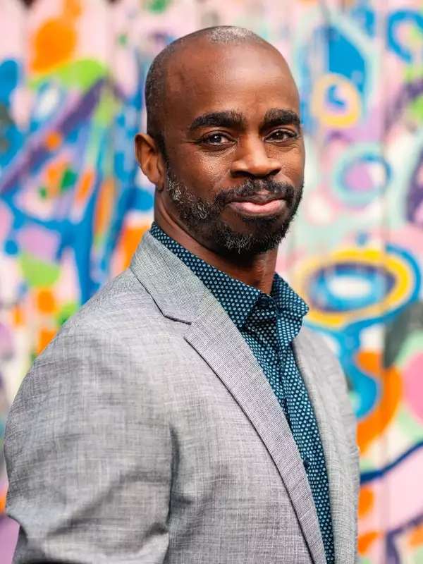 Michael stands in front of a street art wall in a gray suit and smiles at the camera.