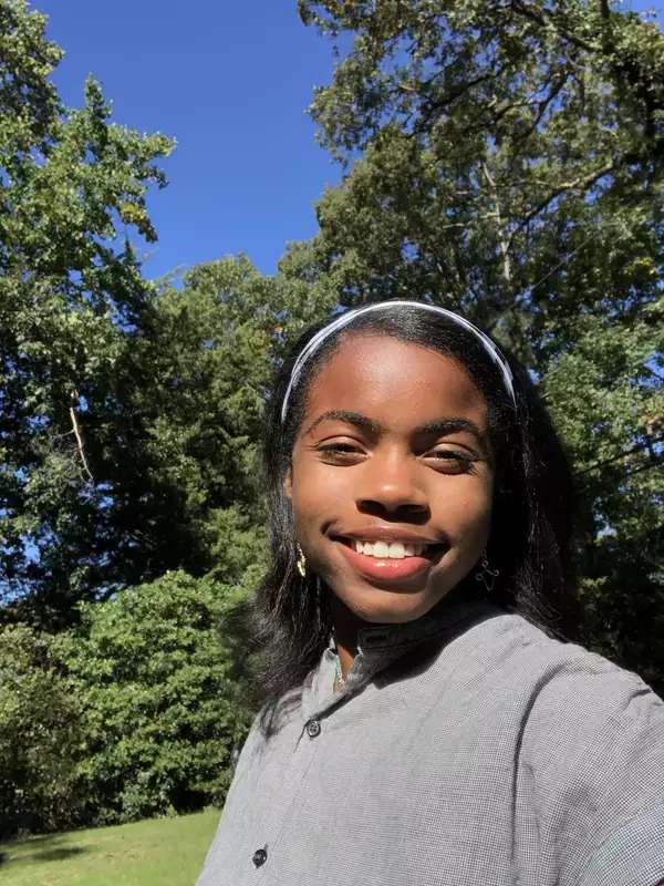 Carter smiling outdoors in front of some trees on a sunny day.