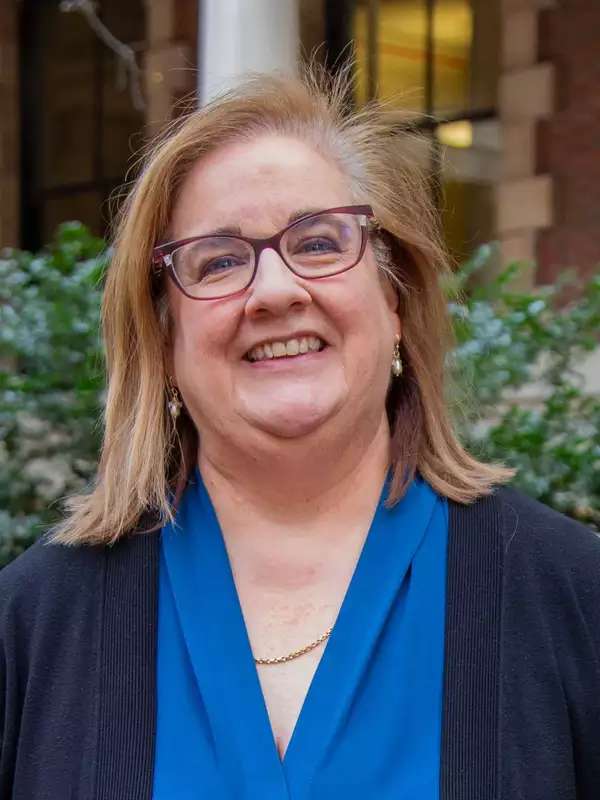 Christine smiling, wearing classes, blue blouse and navy blue sweater against a mixed background