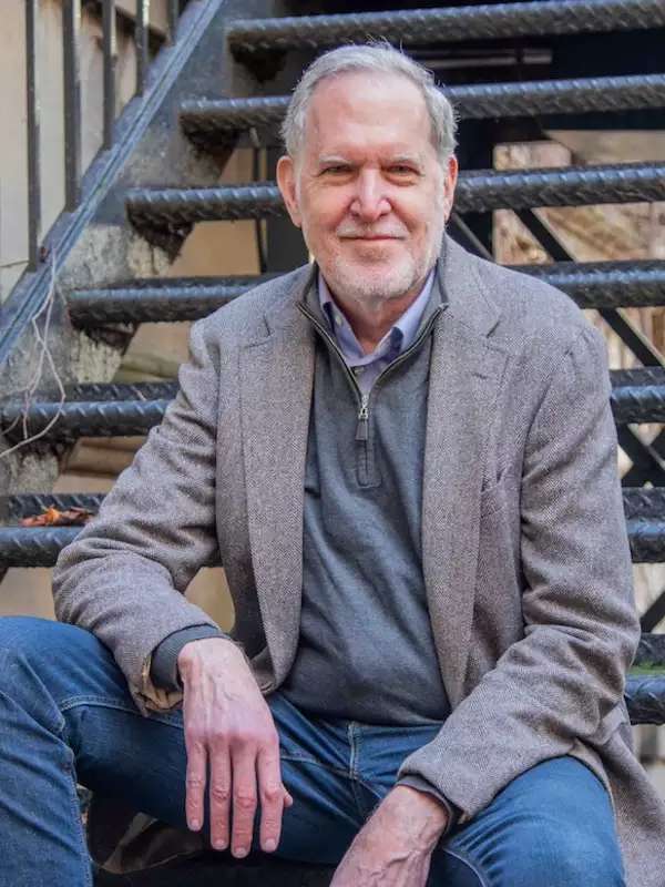 staircase in background, man with gray blazer and blue jeans, close lipped smile