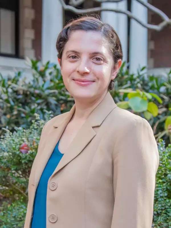 green background, woman wearing light brown blazer, blue shirt and short brown hair