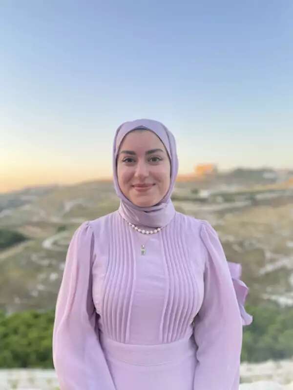 A woman in a pink outfit stands in front of a landscape at sunset. 