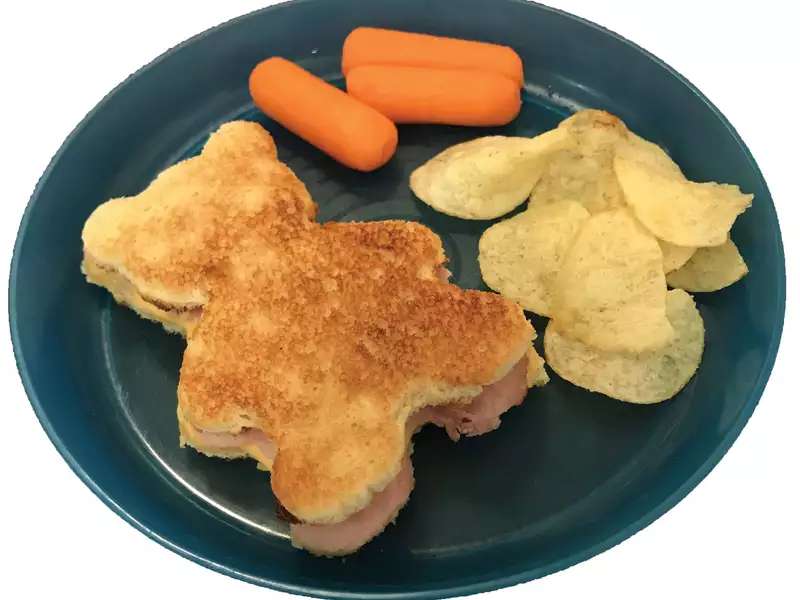 A picture of sandwich shaped like bear with carrots and potato chips. 