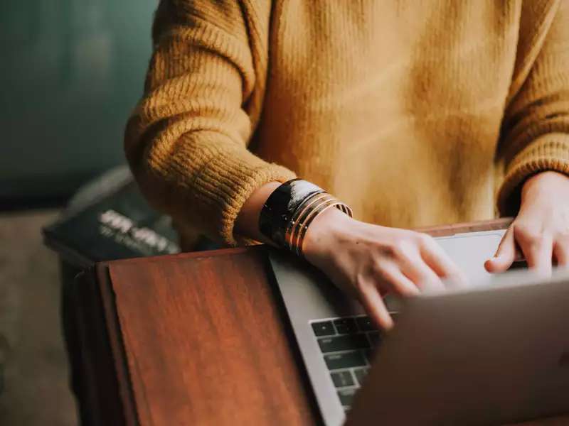 Photo of a person wearing an orange sweater typing at a laptop from the shoulders down