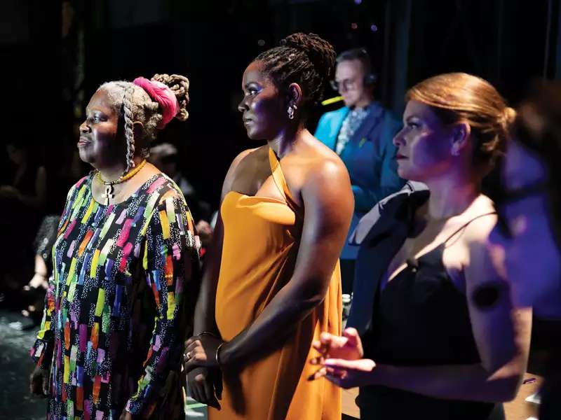 Olivia watkins looking to the left standing on a stage with other women