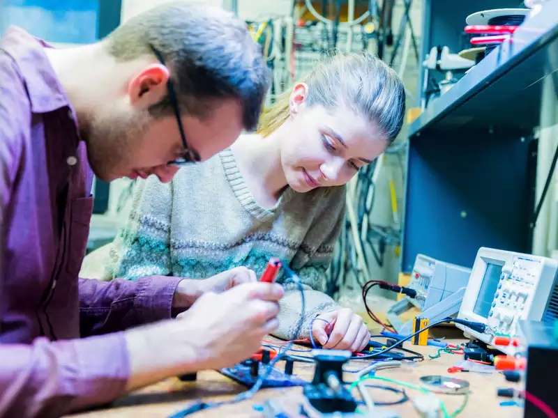 Man and woman working at an electronics bench with engineering tools