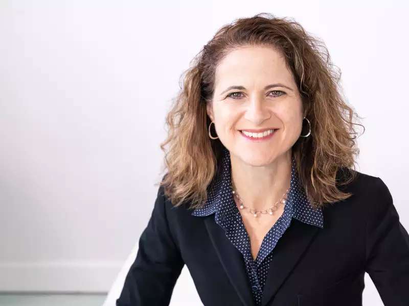 Woman with brown hair wearing black jacket in front of white wall