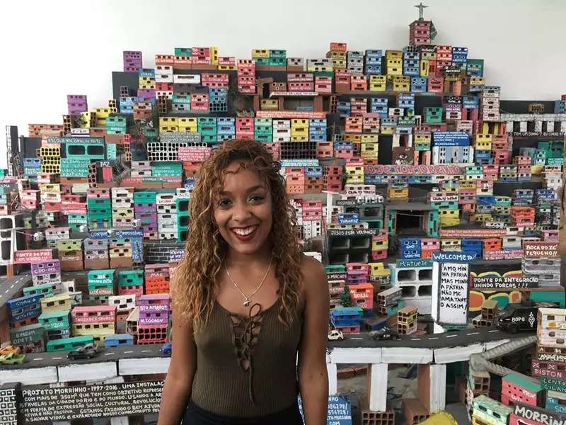 Brown-skinned woman in Rio with colorful models of buildings behind her