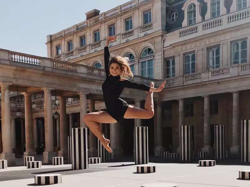 Young woman in a leotard caught mid-leap in city courtyard