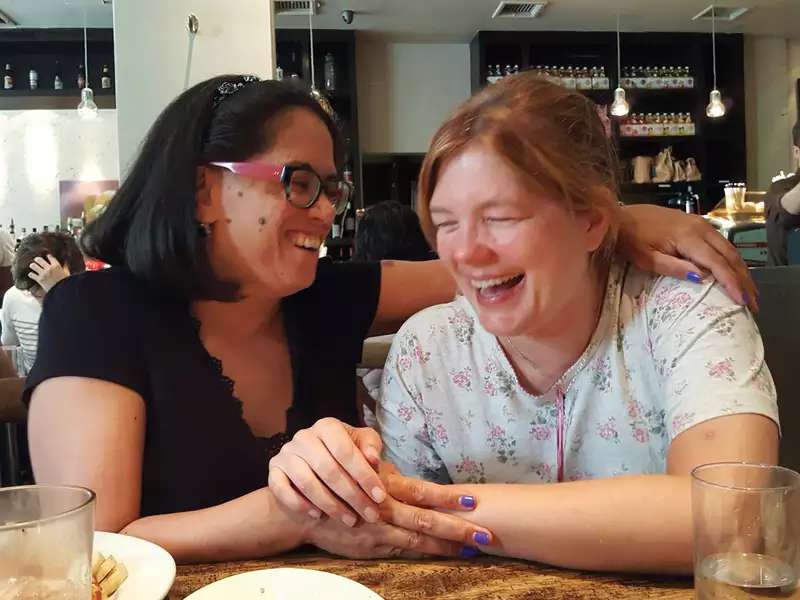 2 women side by side, holding hands and laughing