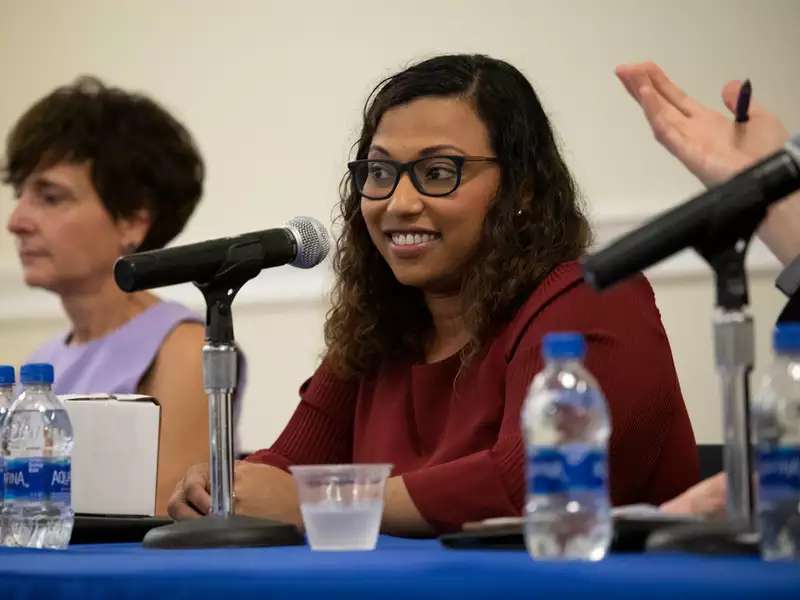 two women seated at a table, speaking on a panel