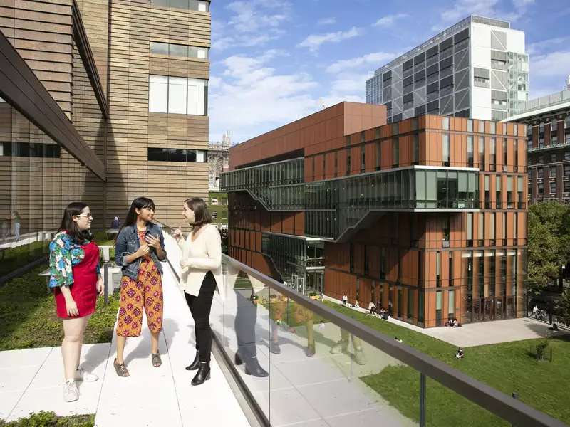 3 students stand on a balcony overlooking Barnard's campus